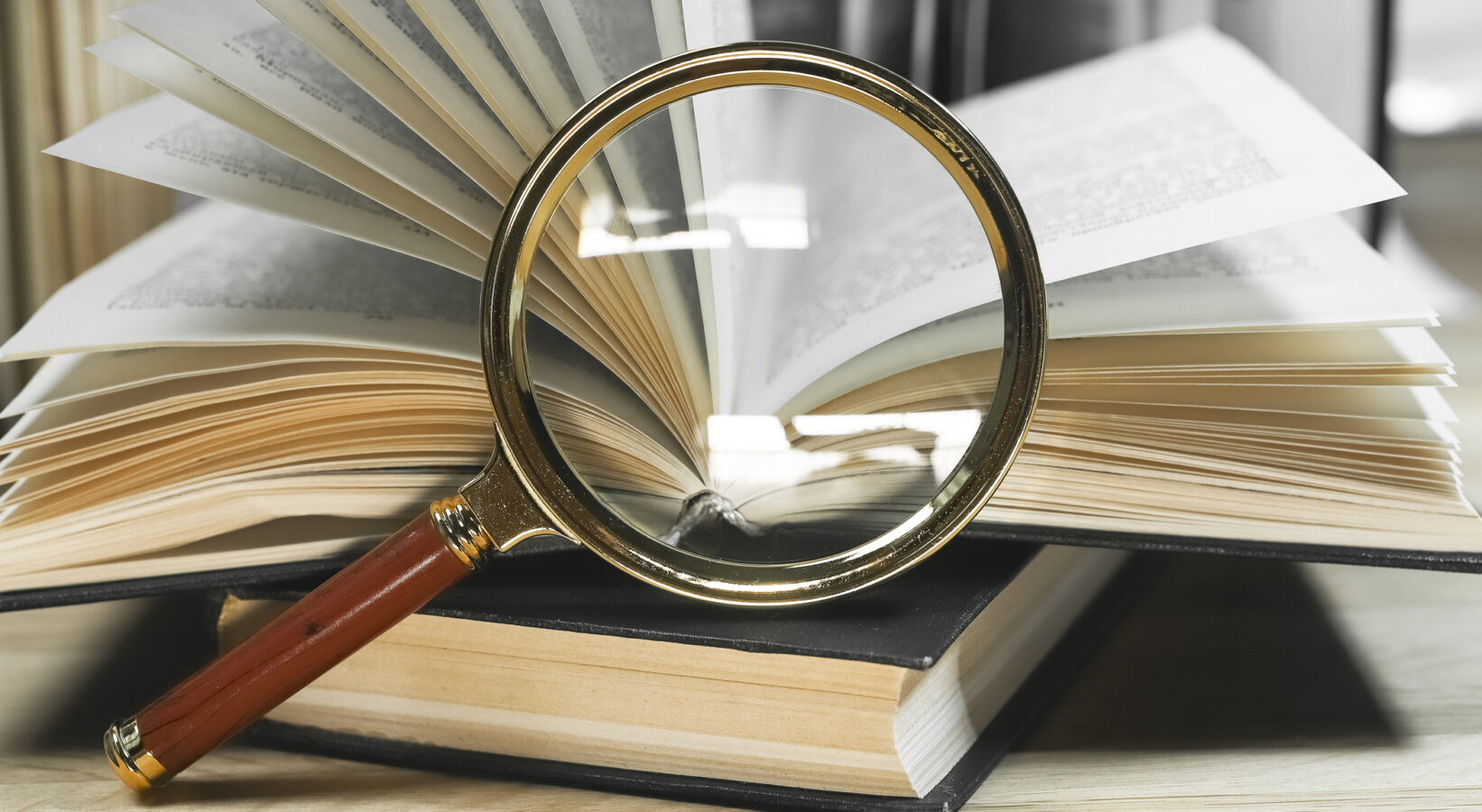 Magnifying lens and open and closed books with turning pages on wooden table. Reading and finding information concept.
